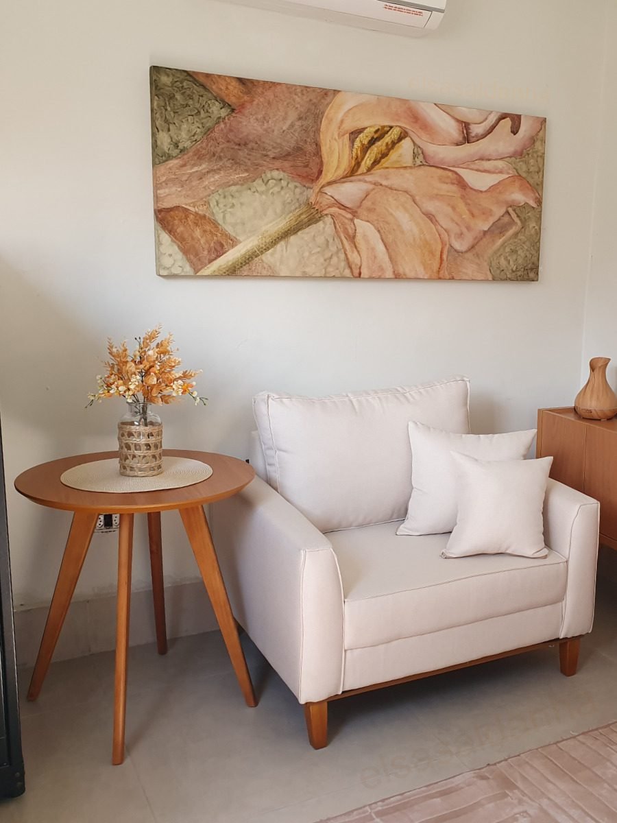 Canto do consultório em Taubaté: poltrona clara, mesa lateral de madeira com um arranjo de flores e um quadro na parede