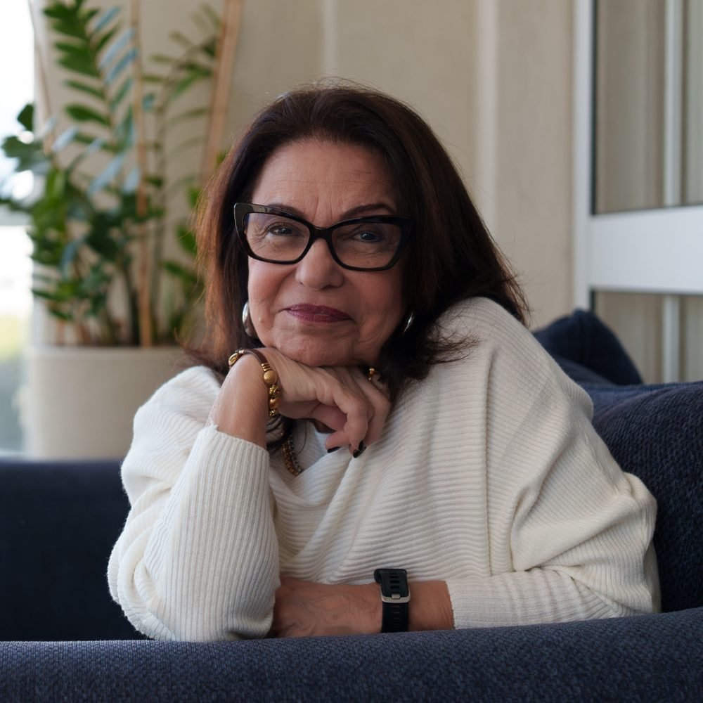 Elsa Saldanha sentada em uma poltrona, com a mão apoiada no queixo